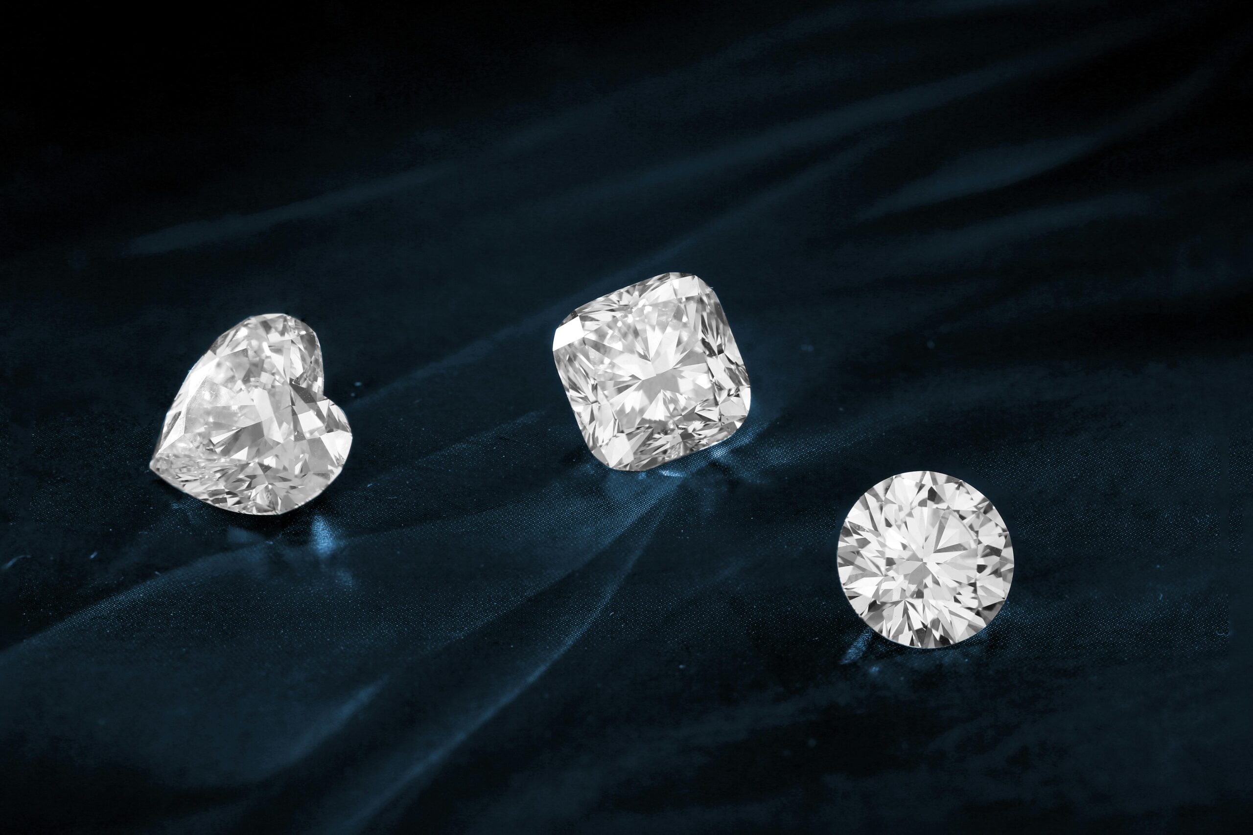 Three exquisite diamonds featuring heart, cushion, and round cuts displayed on dark fabric.